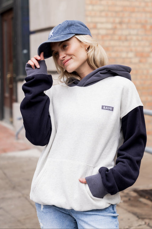 Person wearing a two-tone hoodie and cap outdoors against a brick wall.