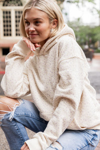 Woman wearing an ivory oversized hoodie with micro lavender floral print and ripped jeans sitting outdoors.