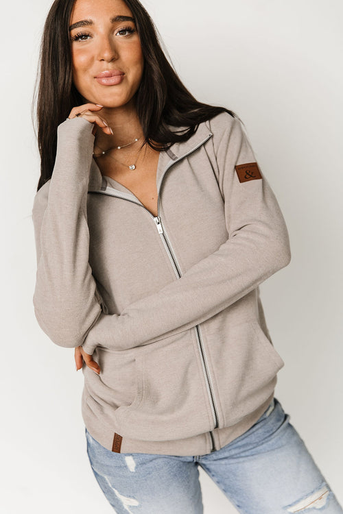 Woman wearing a beige zip-up hoodie with brown accents on a white background